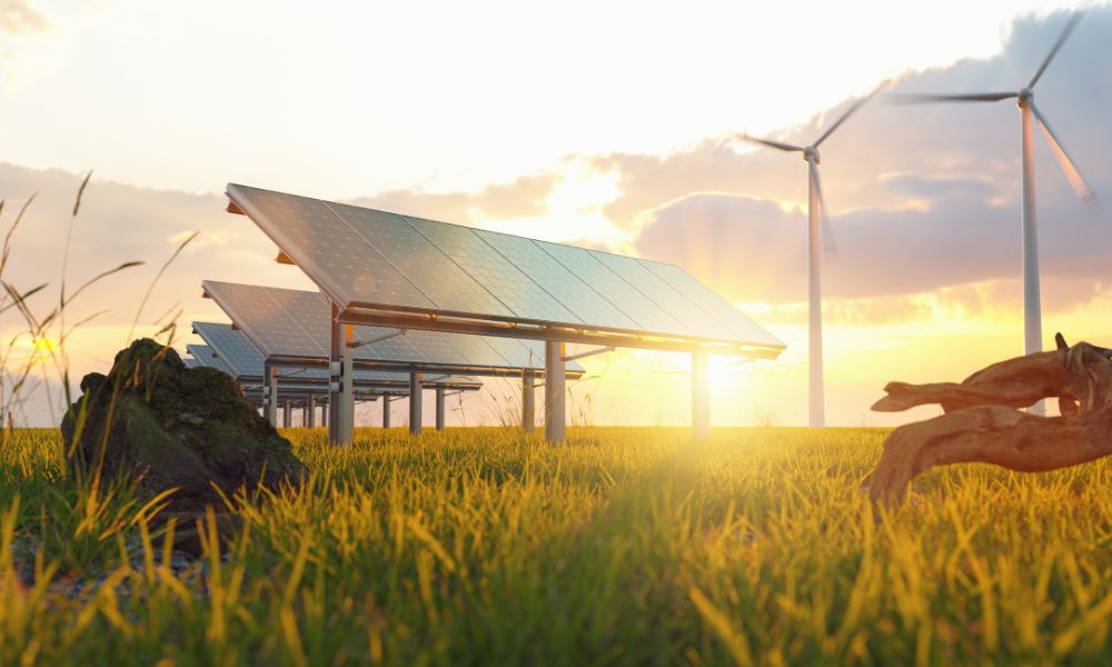 Güneş panelleri ve rüzgar türbinleri, gün batımında çimenli bir alanda yükselerek alternatif enerji kaynaklarının özünü temsil ediyor. Bulutlar tarafından kısmen gizlenen güneş, doğa ve yeniliğin bu uyumlu karışımına sıcak bir parıltı saçıyor.