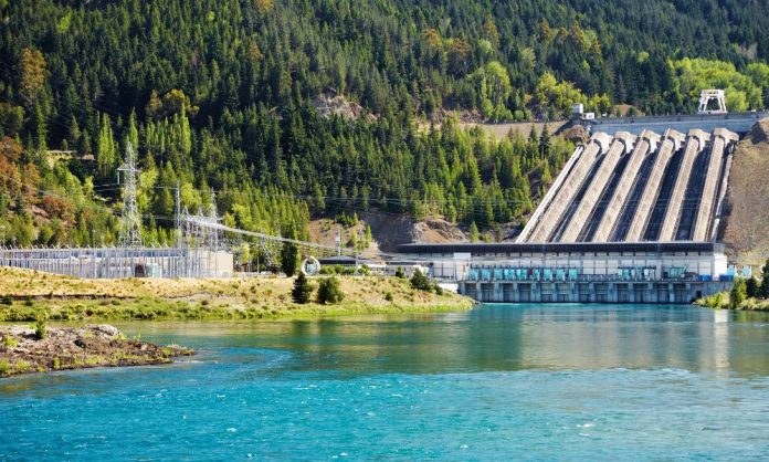 Birden fazla savak bulunan bir hidroelektrik barajı, yemyeşil ormanlar ve tepelerle çevrilidir. Berrak mavi bir su kütlesine bakan bu enerji tesisinin elektrik hatları dışarıya doğru uzanarak doğayı ve teknolojiyi kusursuz bir şekilde bütünleştirir.